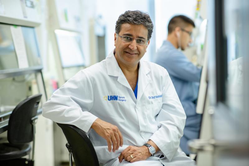 Shaf Keshavjee smiles, wearing a lab coat with the logo: UHN Sprott Surgery