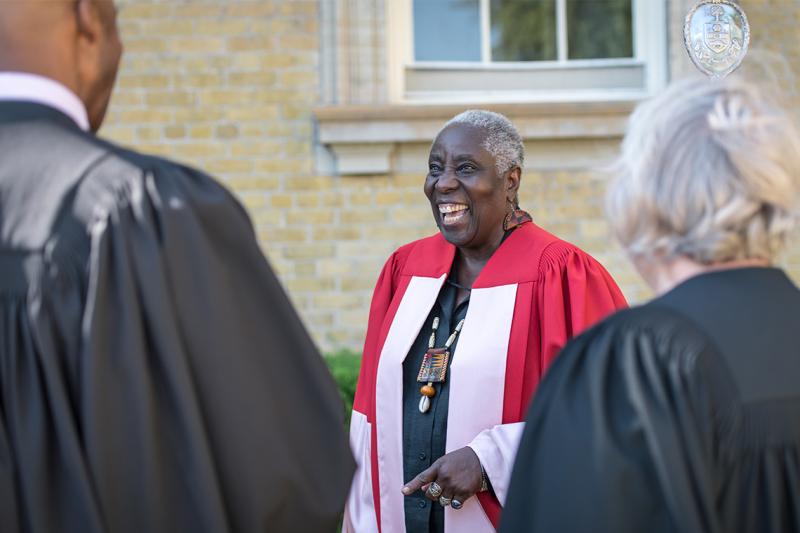 Camille Orridge, wearing academic robes, laughs out loud as she chats with other academics in robes.