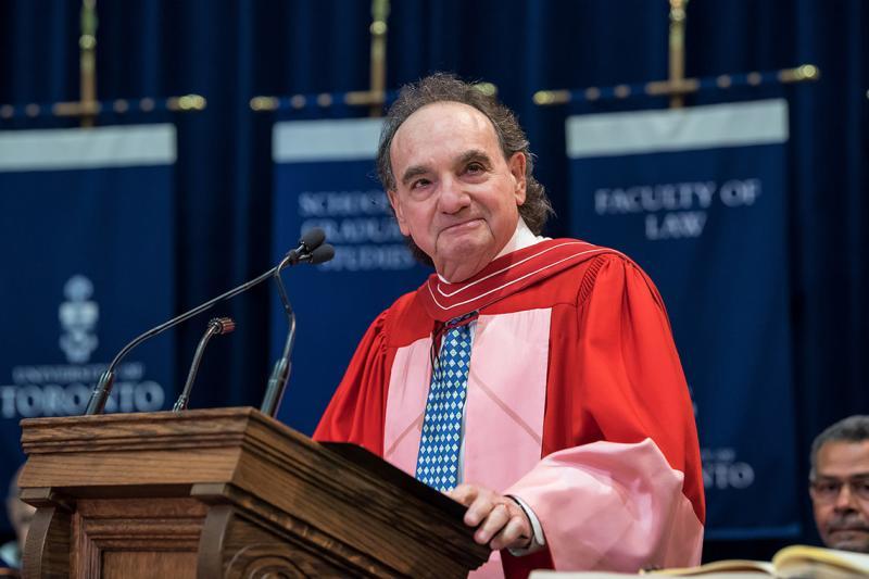 Michael Moldaver, wearing academic robes, smiles from the podium at Convocation Hall.