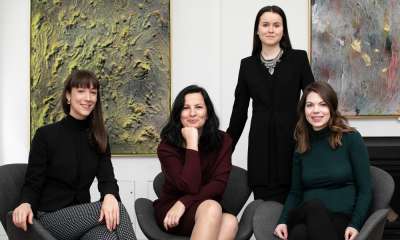 Four women smile as they sit together in a room hung with artworks.