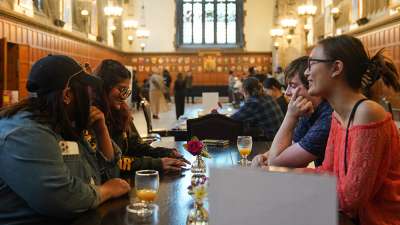 Four students sitting together at a table at Hart House, talking and smiling.