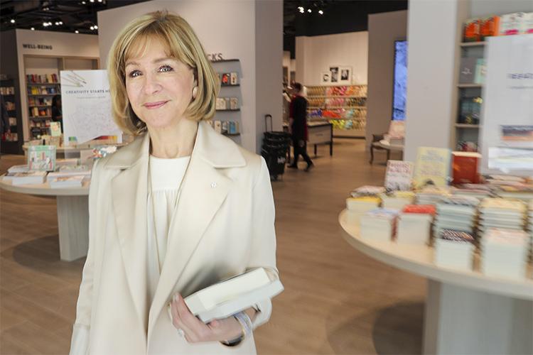 Heather Reisman smiles, holding books and standing in a bookstore.