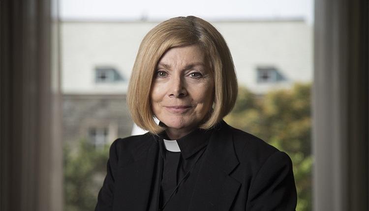 Cheri DiNovo, wearing her clerical collar, smiles while sitting by a window.