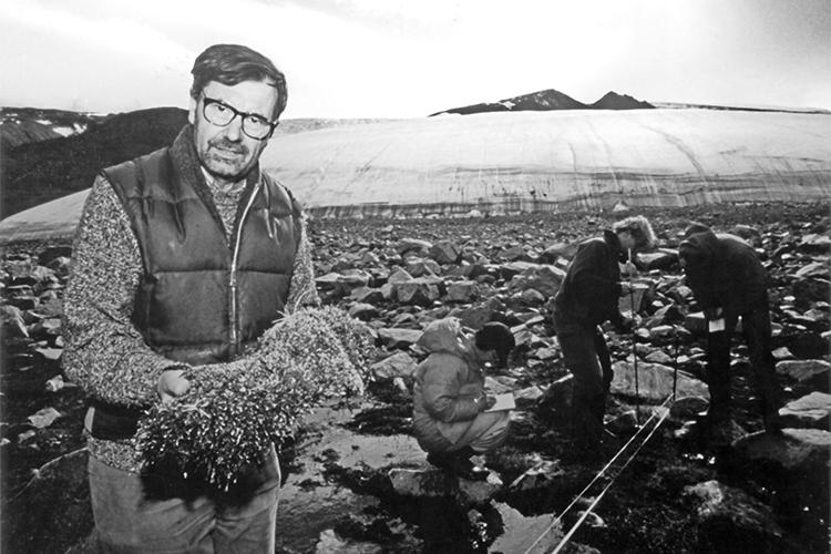 Josef Svoboda holds a clump of moss as he stands on rocks in front of a glacier.