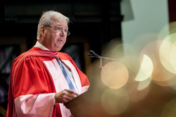 Carlo Fidani, wearing academic robes, speaks at a lectern in Convocation Hall.