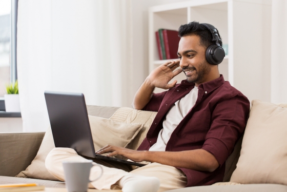Man sits on couch using laptop and listening through headphones, smiling