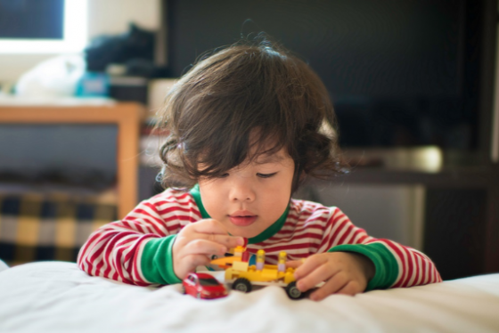 Child playing with a toy truck and car on a bed.