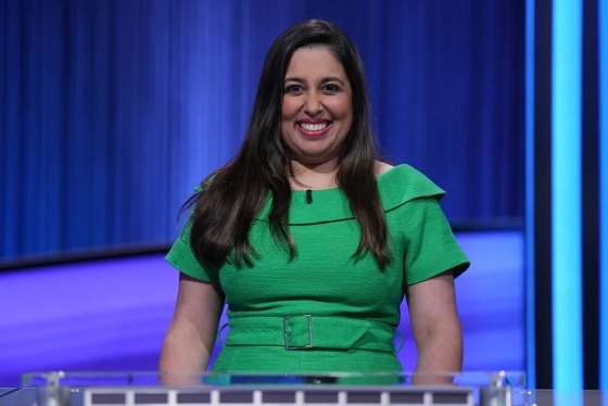 Javeria Zaheer wearing a green dress and smiling on the Jeopardy! set.
