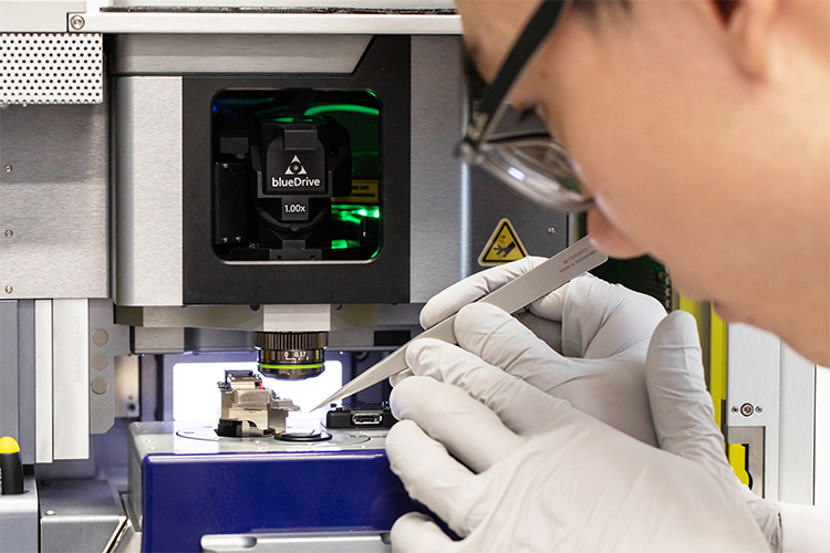 Teng Cui uses tweezers to place a graphene chip under the lens of a microscope