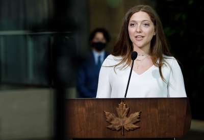 Lana El Sanyoura speaks at a podium emblazoned with a carved wooden maple leaf.