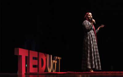 Salma Hindy talks into a microphone on a stage. Large letters behind her read, TED U of T.