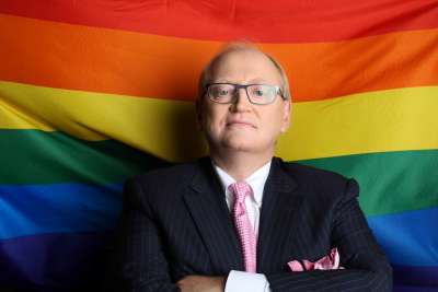 Photo of R. Douglas Elliott in front of a rainbow flag.