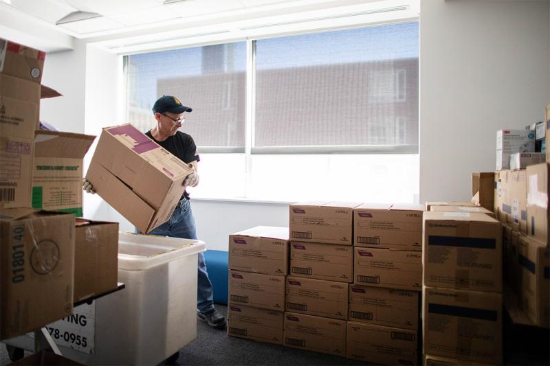 A man lifts a cardboard box and adds it to a large pile of other boxes.