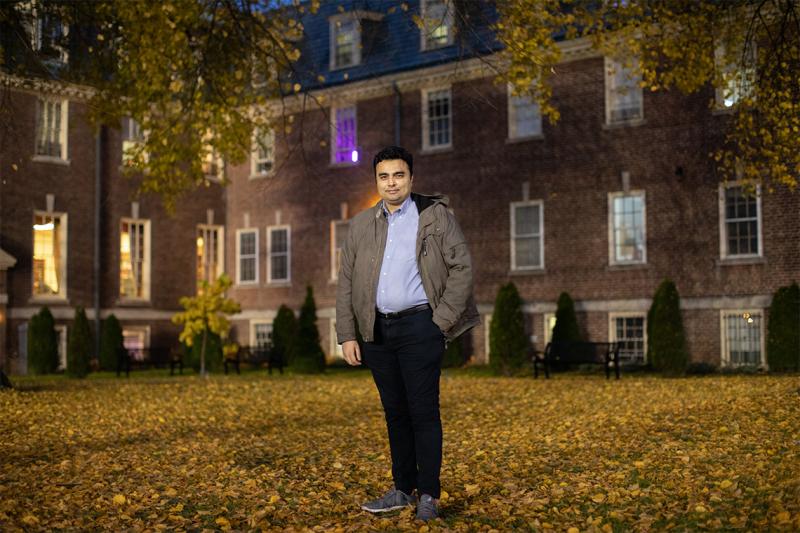 Saad Shahid Shafiq smiles as he stands in a  leafy U of T quad at night.