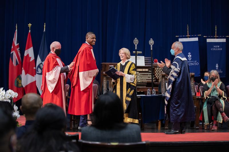 Masai Ujiri smiles as university officials place his academic hood over his head, on stage at Convocation Hall.