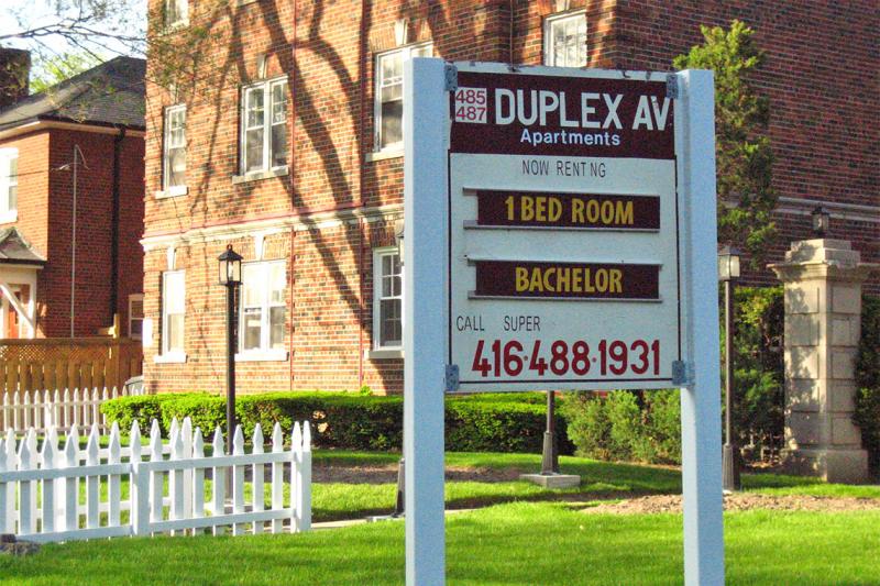 A sign outside a brick building reads: 485/487 Duplex Ave, now renting, 1 bedroom, bachelor, call super 416-488-1931.