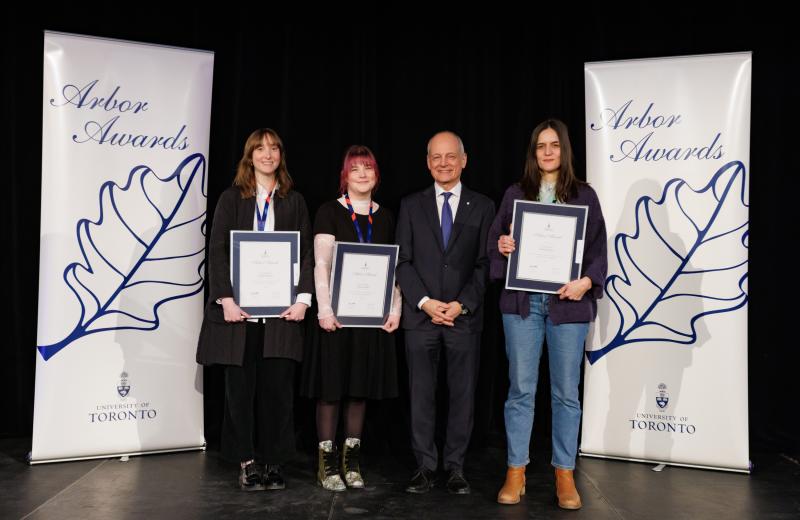 Three awards winners standing together with U of T president Meric Gertler, smiling and holding their awards..