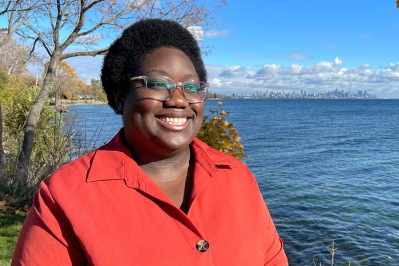 Marquela Nunes smiles happily, standing on the shores of a lake.