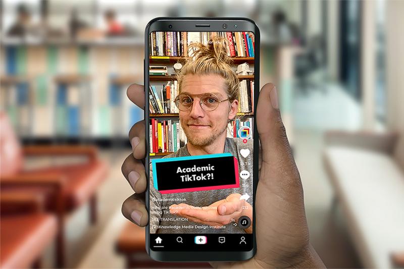 A hand holds a smartphone. On the screen, a young man makes a wry face. A text caption reads: Academic TikTok?!