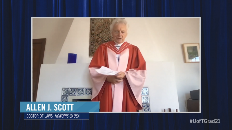Allen J Scott, wearing academic robes, speaks from written notes while standing in front of a tiled fireplace.