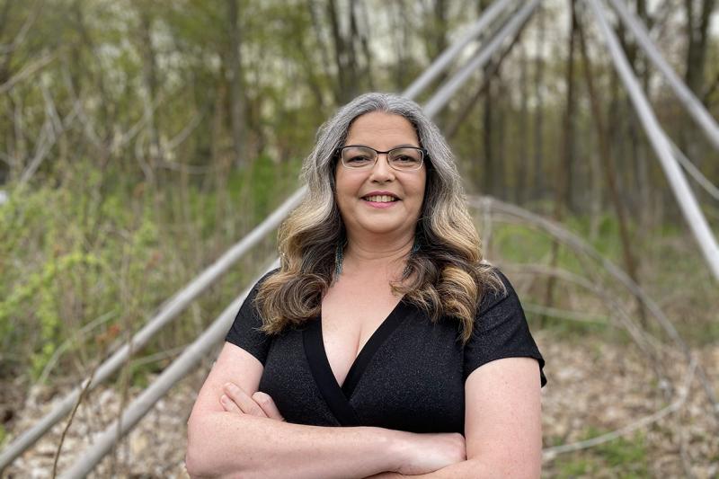 Angela Mashford-Pringle smiles as she stands outdoors in a forest.