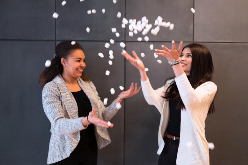Anne Ageh and Nuha Siddiqui laugh together as they toss biodegradable packing peanuts in the air.