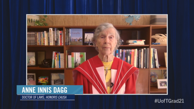 Anne Innis Dagg, wearing her academic robes and hood, speaks on video in front of a bookcase.