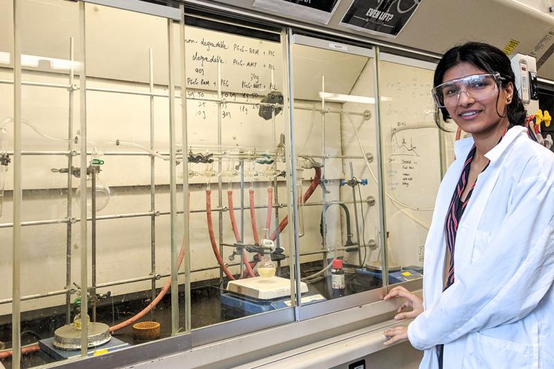 Avneet Ghotra, wearing safety goggles and lab coat, stands in front of an array of taps, hoses, beakers and clamps.