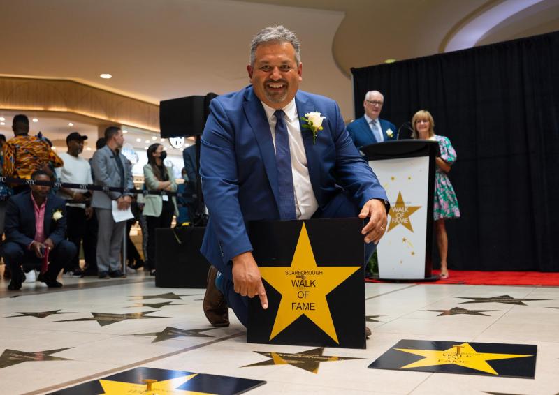 Andrew Arifuzzaman smiles happily, kneeling on a pavement with star-shaped tiles: Scarborough walk of fame.