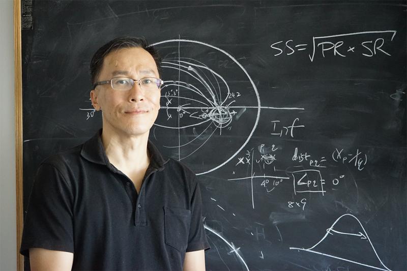 Willy Wong stands in front of a blackboard covered with an oval-shaped diagram and mathematical formulae.
