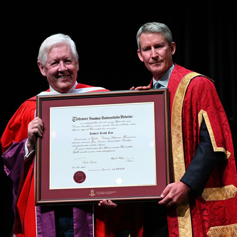 Bob Rae poses with Victoria University Chancellor Nick Saul and a large framed diploma.