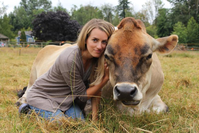Camille Labchuk  hugs a cow that is lying crouched in a field.