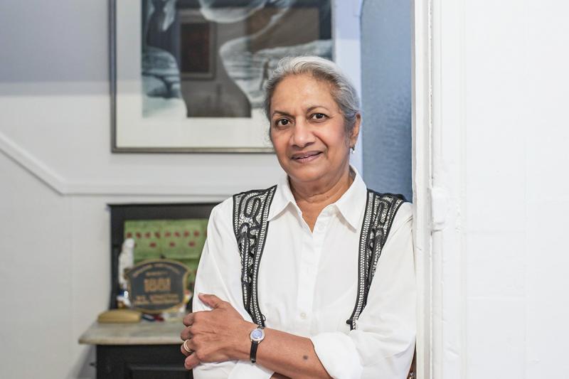 Ceta Ramkhalawansingh smiles, leaning in a doorway near a desk holding memorabilia.