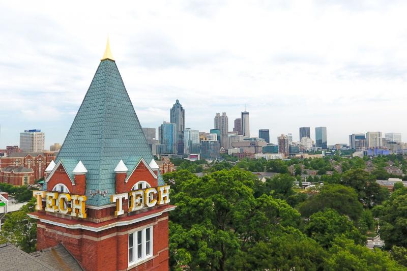The word TECH is blazoned on the roof of a tower overlooking a forested city campus.