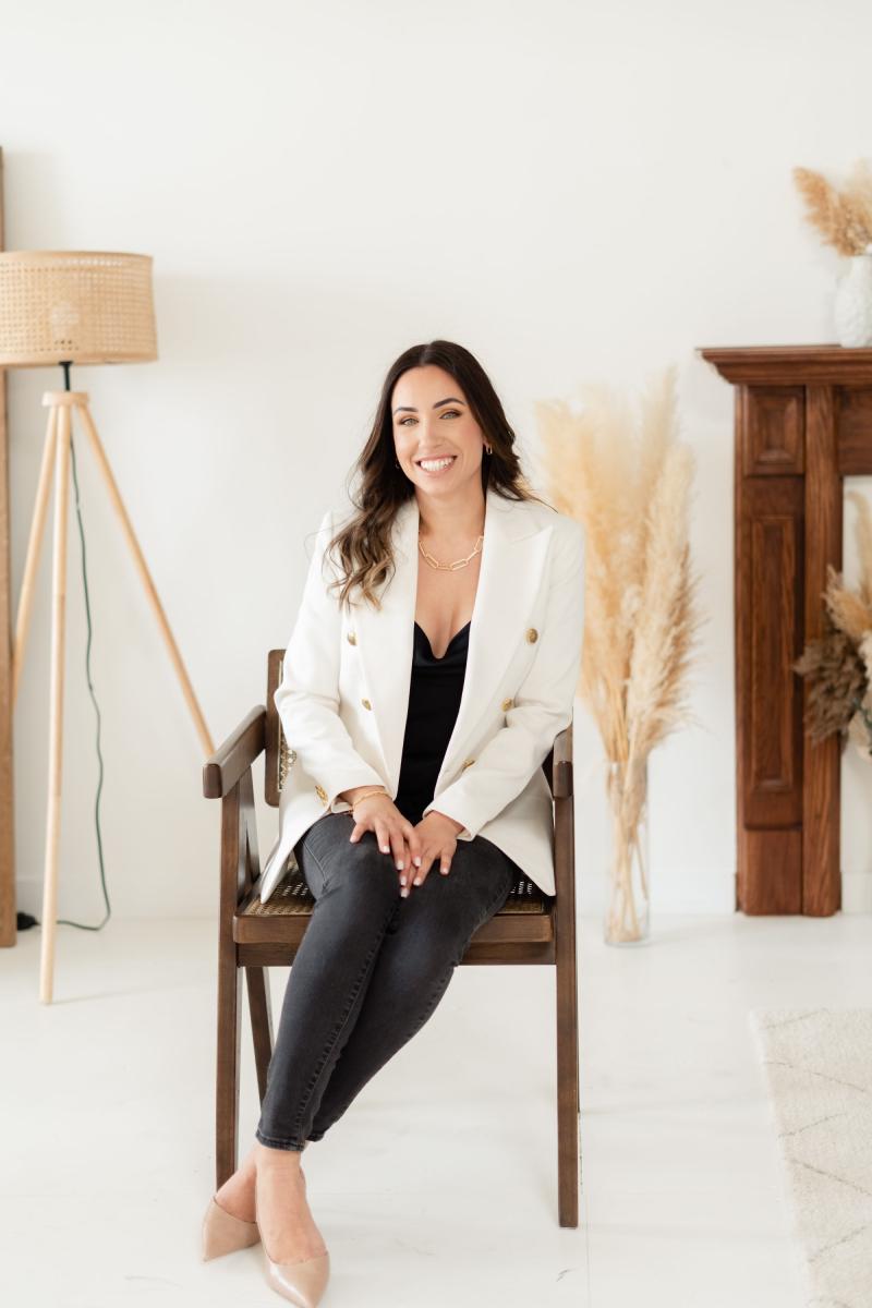 Portrait of Lauren Watkins sitting in a chair and wearing a white blazer