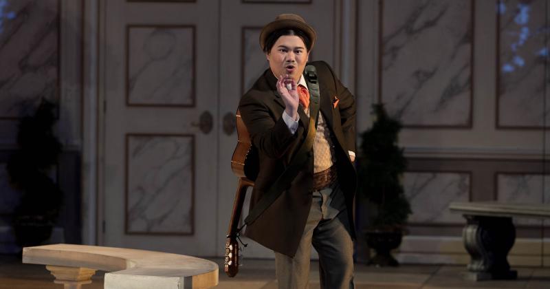 Danlie Rae Acebuque in costume as Figaro. He is singing and gesturing, wearing a guitar slung on his back.