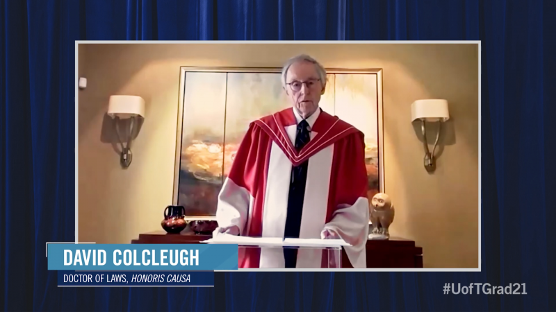 David Colcleugh, wearing his academic robes and hood, speaks on video in a room with an elaborate fireplace.