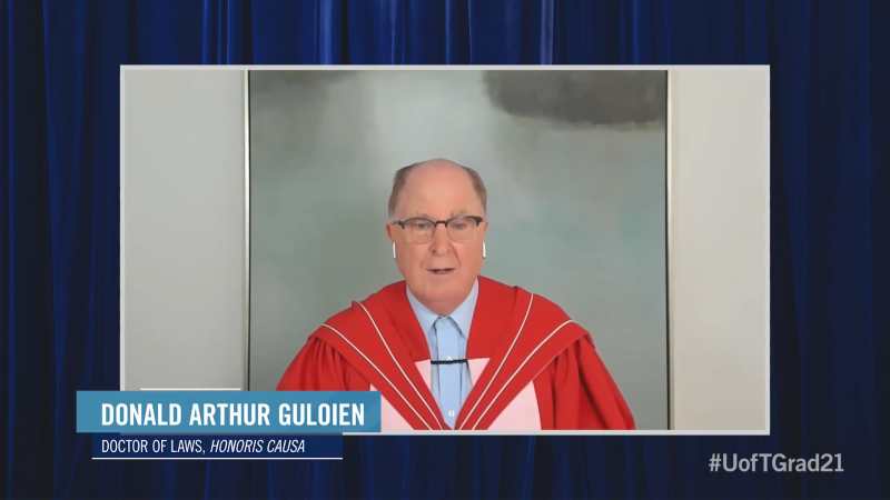 Donald Guloien, wearing academic robes, speaks while standing in front of an oil painting.