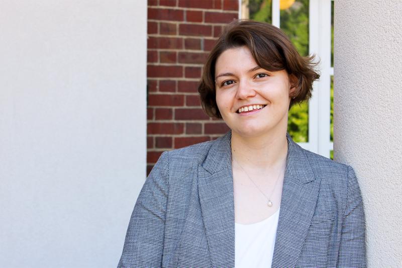 Ema Ibrakovic smiles, standing on a porch outdoors.