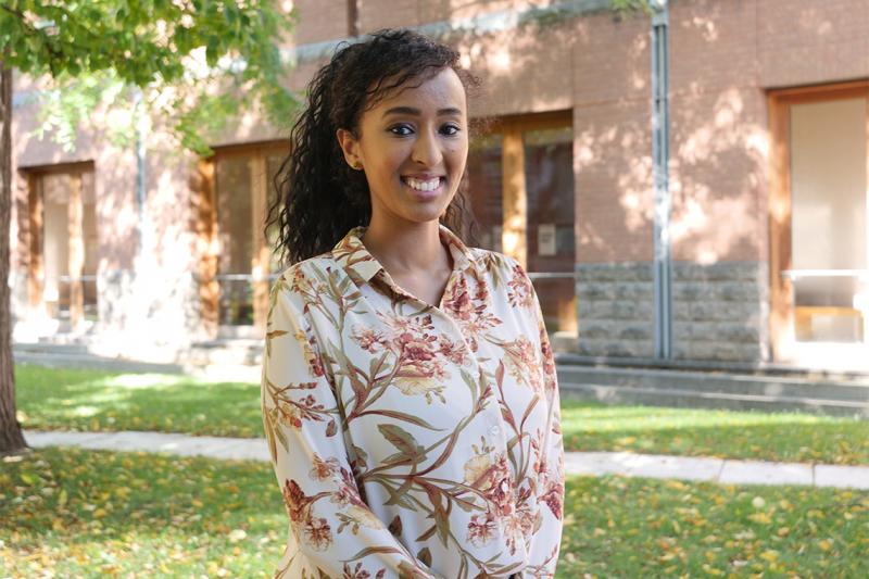 Entisar Yusuf smiles as she stands in a sunny courtyard under a tree.