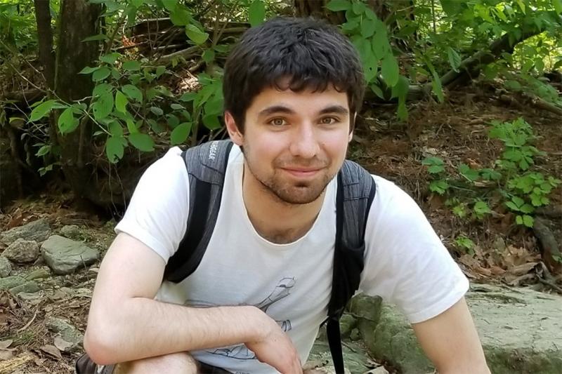 Erik Etzler smiles as he crouches on a forest trail, wearing a backpack.