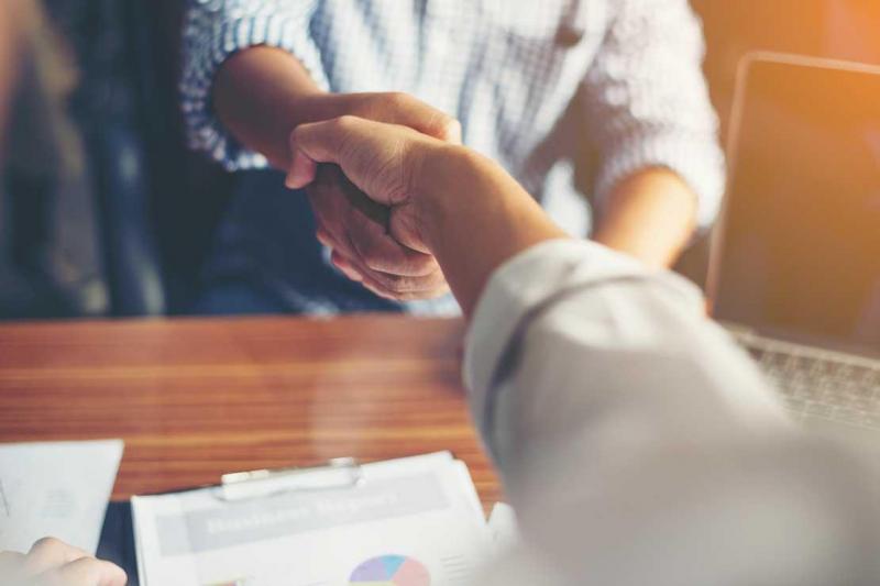 Picture of the arms and hands of two people shaking hands across a wooden desk.