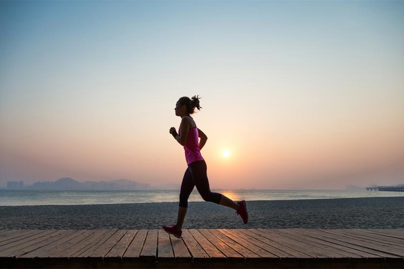 A woman runs along an empty beach at sunset.