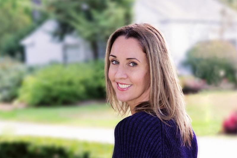 Natalie Jenner looks over her shoulder and smiles, standing beside a residential street.