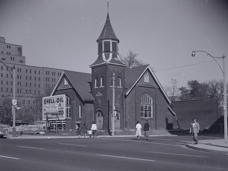 Archival photograph of First Baptist Church in the 1950s, squeezed next to a construction site and a billboard for Shell Oil.