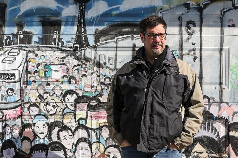 Colin Furness stands in front of a wall mural that shows a crowded streetcar platform.