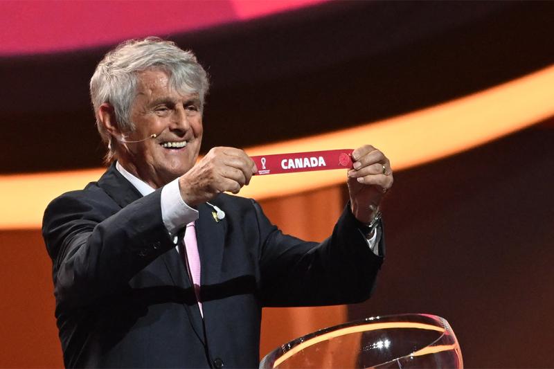 Former Serbian footballer Bora Milutinović smiles and holds up a strip of paper with text reading: Canada.
