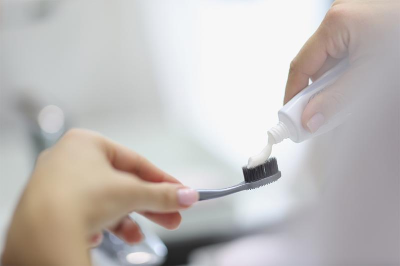 A close-up of a person's hands as they squeeze toothpaste onto a toothbrush.