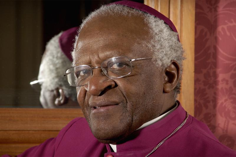 Archbishop Desmond Tutu smiles quietly. He wears a formal skullcap and gown.