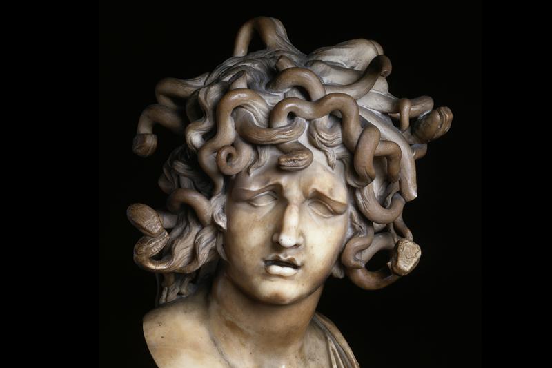 An ancient stone statue of Medusa shows a woman with no eyes and hair made of writhing snakes.